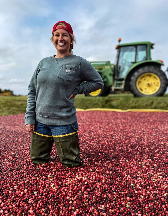 A farmer stands in a flooded cranberry bog with a tractor in the distance.